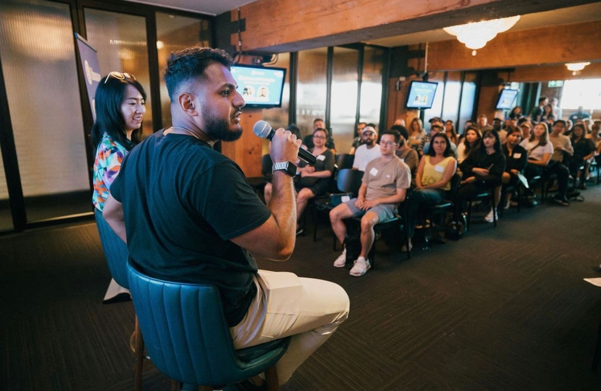 Man speaking with a microphone to an audience seated in a conference room.